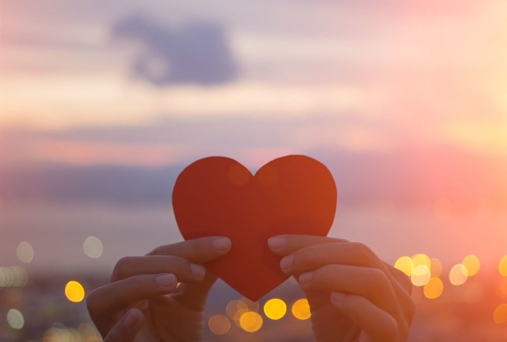 person holding red paper heart in the sun