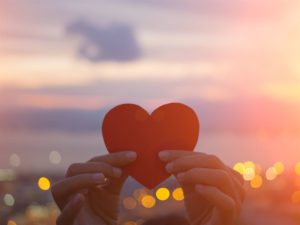 person holding red paper heart in the sun