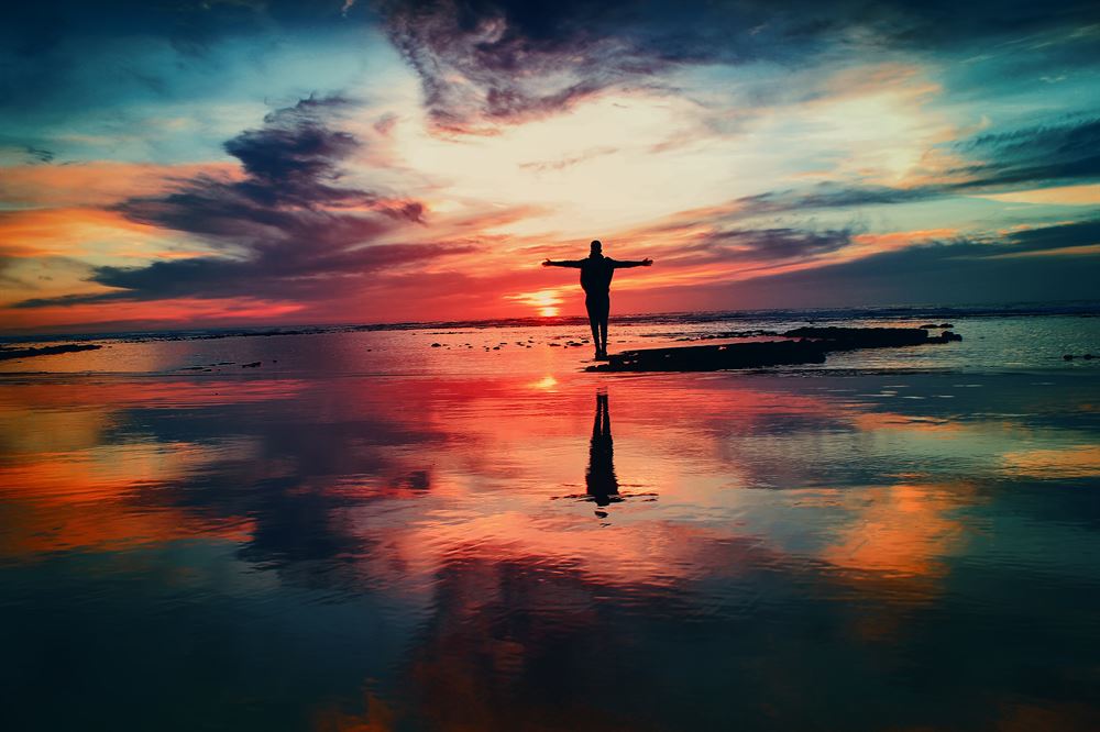 silhouette of person with outstretched arms on a beach during sunset
