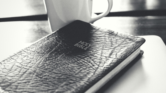 holy bible sitting on a desk next to a cup of coffee