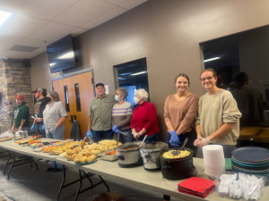 Volunteers from Heart of Longmont stand behind a row of tables set to serve clients at HOPE supper