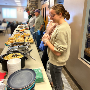 Volunteers stand behind a table loaded with food to serve supper to HOPE clients