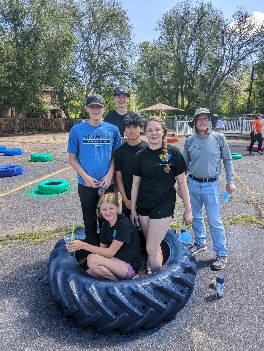 A photo of HOL youth group members in a large tire in front of tires that have been painted in the HOL parking lot for the outdoor learning center